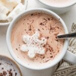 Close up overhead view of two mugs of homemade hot cocoa, from a chocolate cream base, served with snowflake-shaped marshmallows and chocolate shavings.