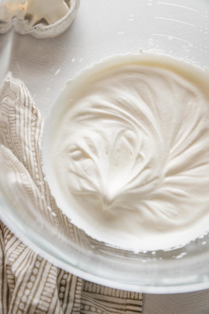 Cream whipped to soft peaks in a clear glass mixing bowl.
