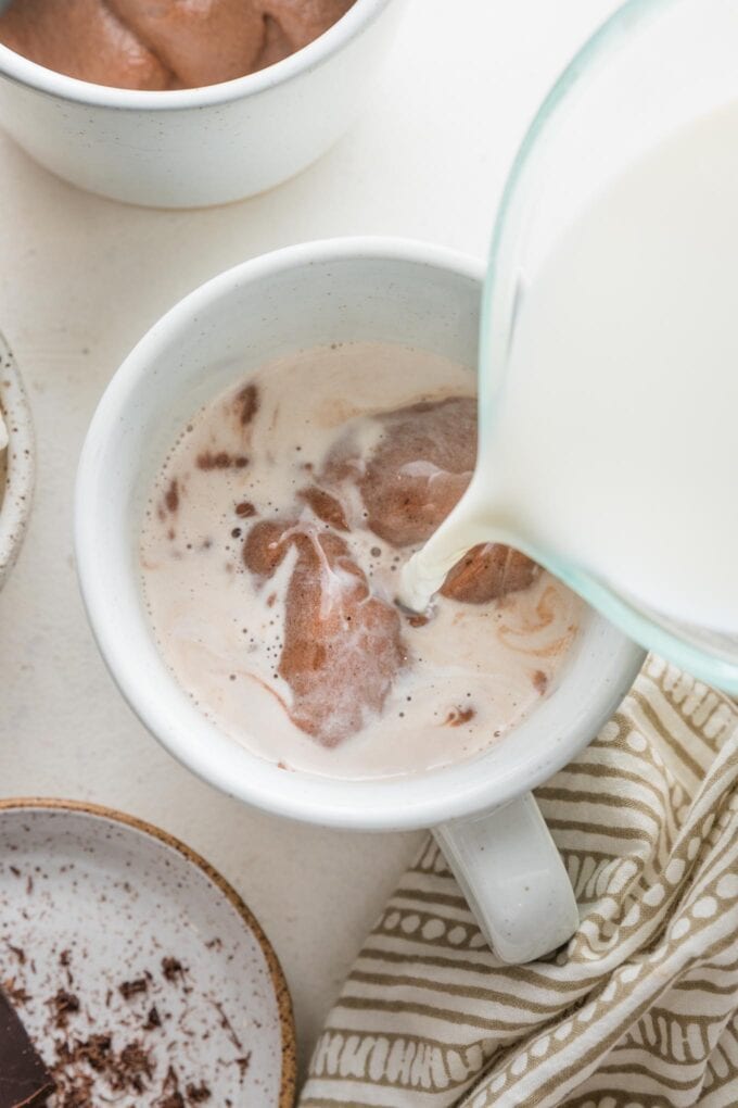 Action shot of warm milk being poured over hot cocoa mix in a mug.