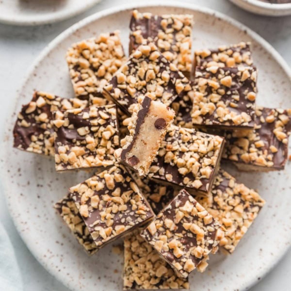 Plate of chocolate coated shortbread toffee cookie bars, with one turned to show the layers.