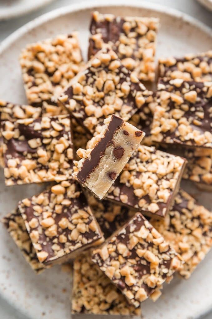 Close up of a layered cookie bar with a chocolate chip-studded shortbread base, chocolate coating, and toffee bits on top.
