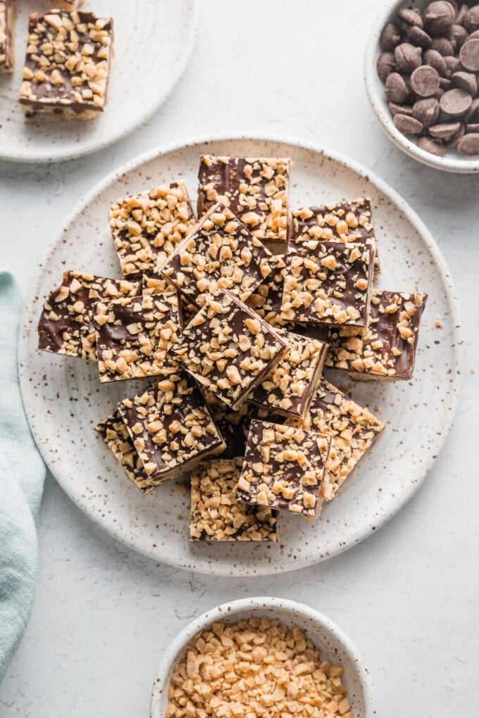 Small plate piled with shortbread toffee cookie bars, with extra toffee bits and chocolate chips in the background.