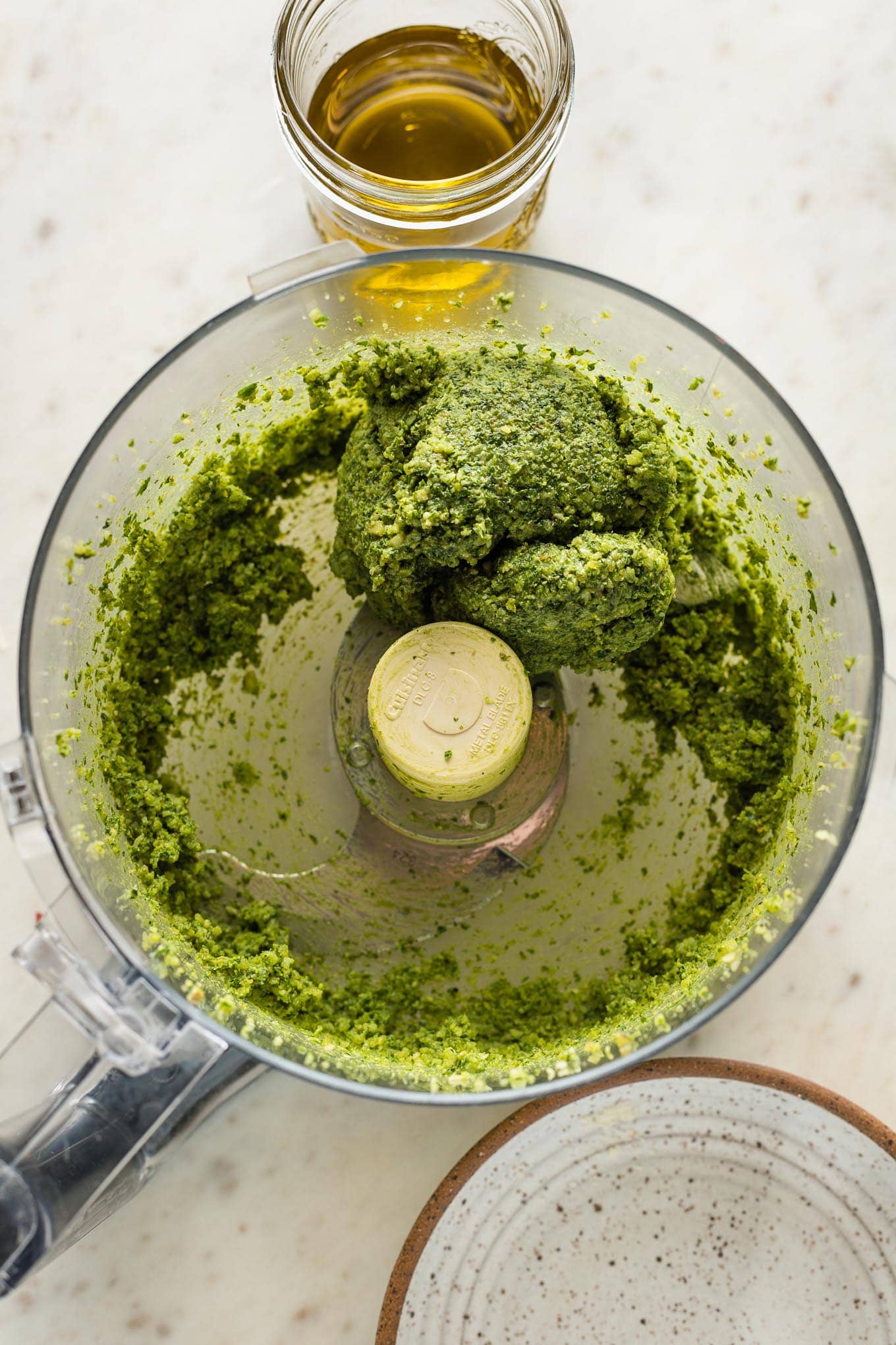 Basil pesto forming a clump in the food processor before olive oil is added.
