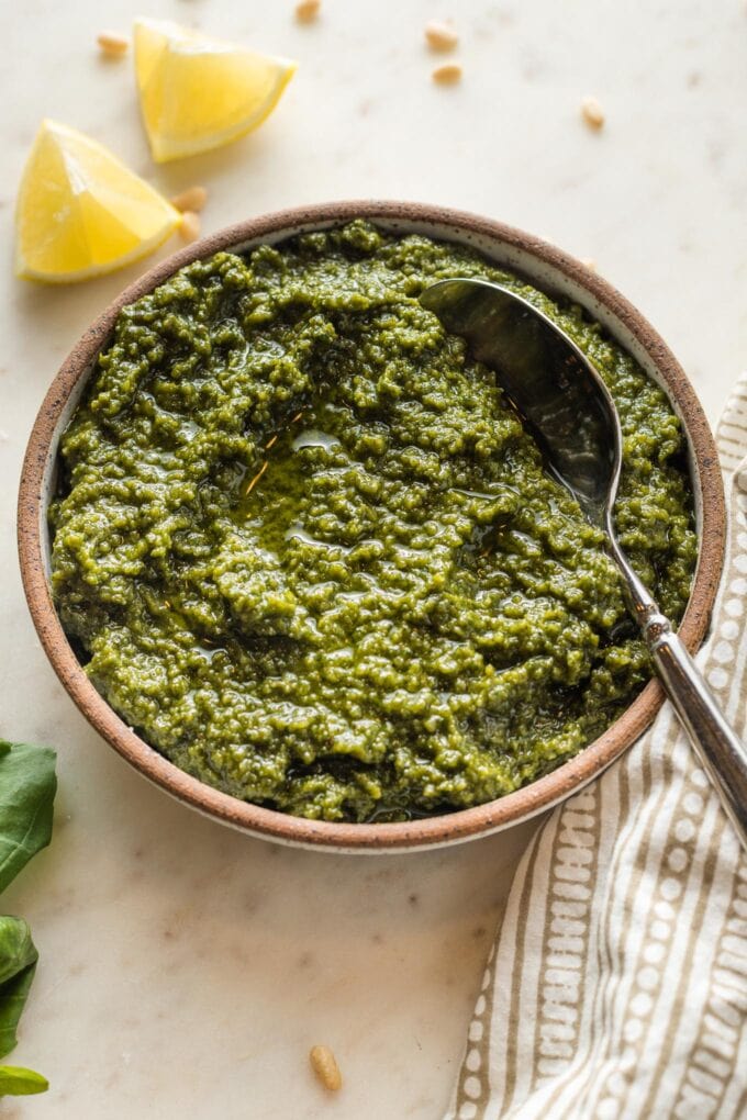 Close up view of basil pesto in a bowl with lemon wedges in the background.