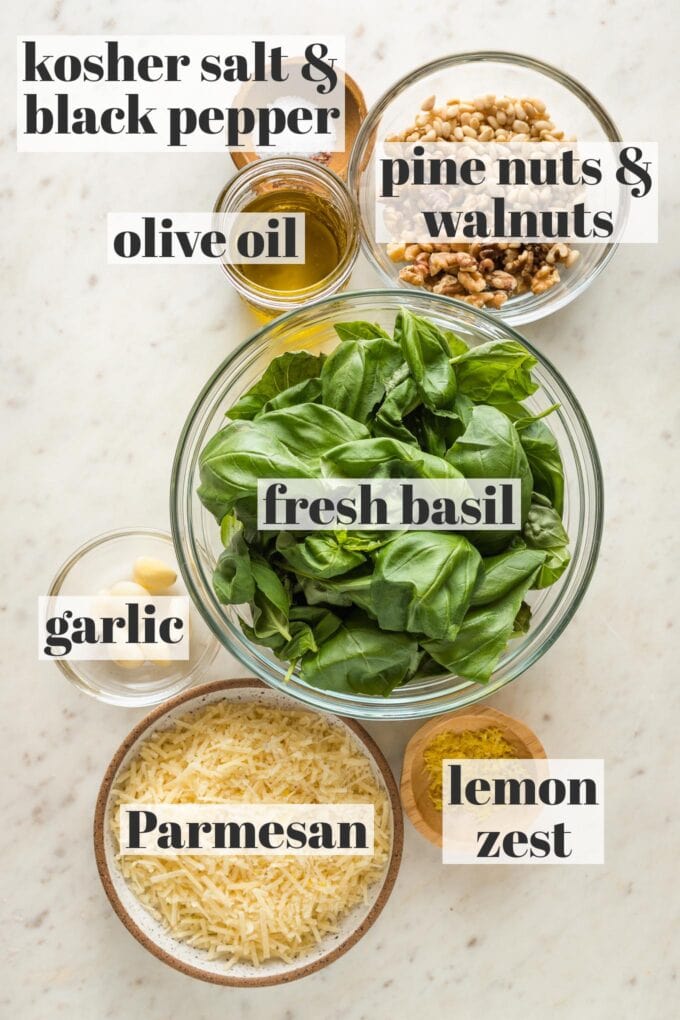 Prep bowls holding fresh basil leaves, garlic, pine nuts, walnuts, salt and pepper, Parmesan, and lemon zest.