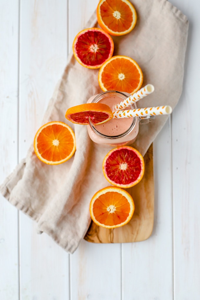 Flat-lay photo of a blood orange banana smoothie, surrounded by bright orange and red slices of citrus.