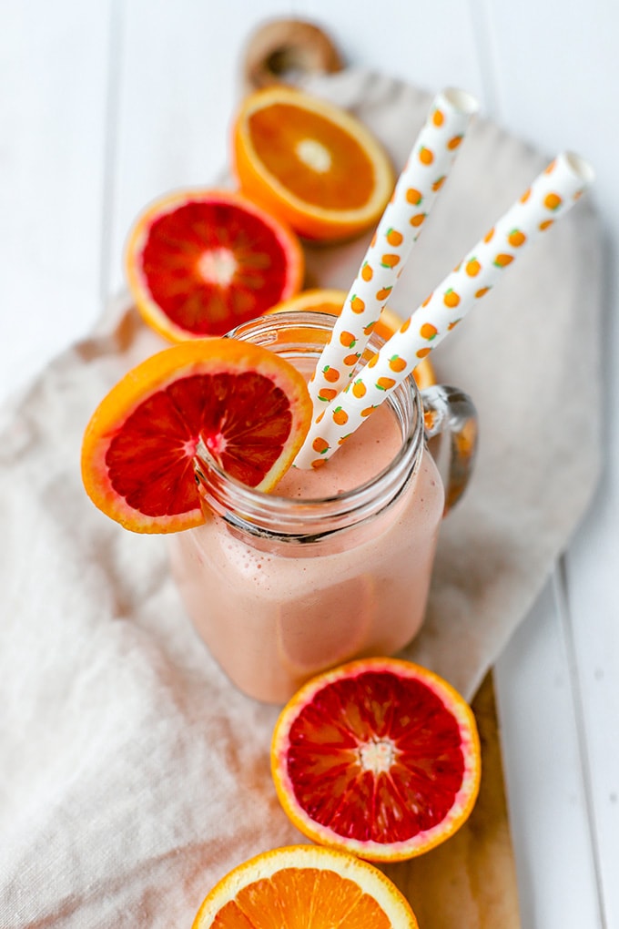 A bright pink blood orange banana smoothie, served in a mason jar with two straws.