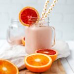 A bright pink blood orange banana smoothie, served in a mason jar with two straws.