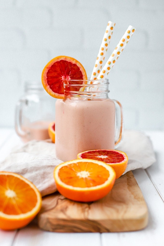 A bright pink blood orange banana smoothie, served in a mason jar with two straws.