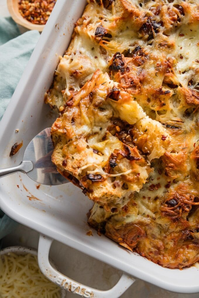 Wood-handled serving spatula lifting a square of breakfast strata out of a large pan.