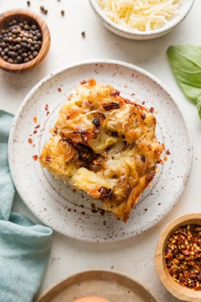 Small plate with a square of breakfast strata, garnished with red pepper flakes and extra cheese.