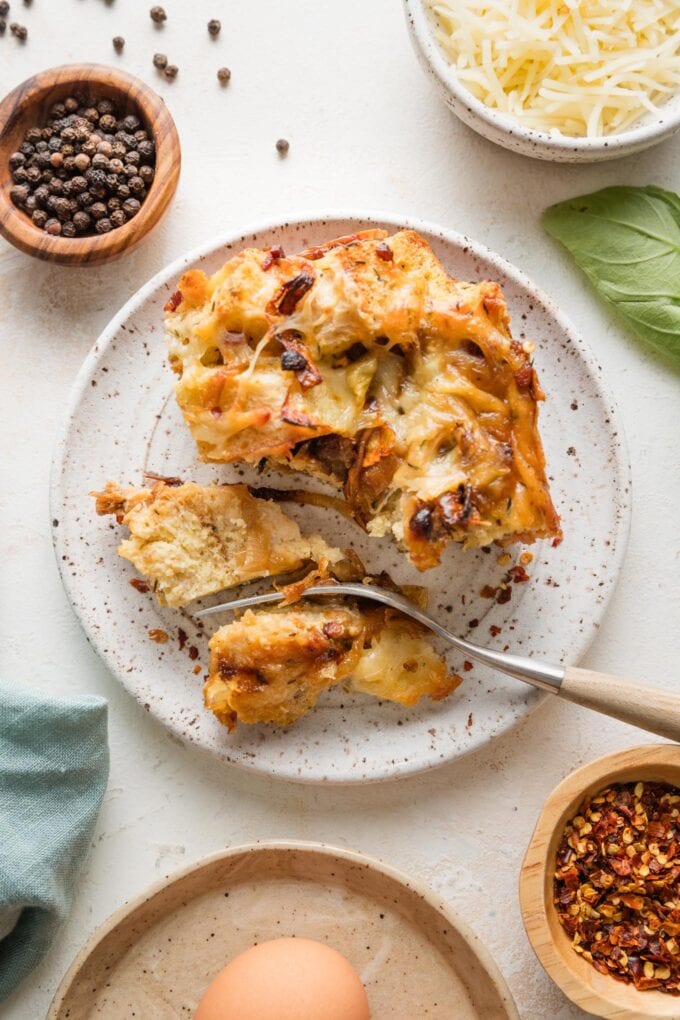 Fork taking a bite of breakfast strata from a piece served on a small plate.