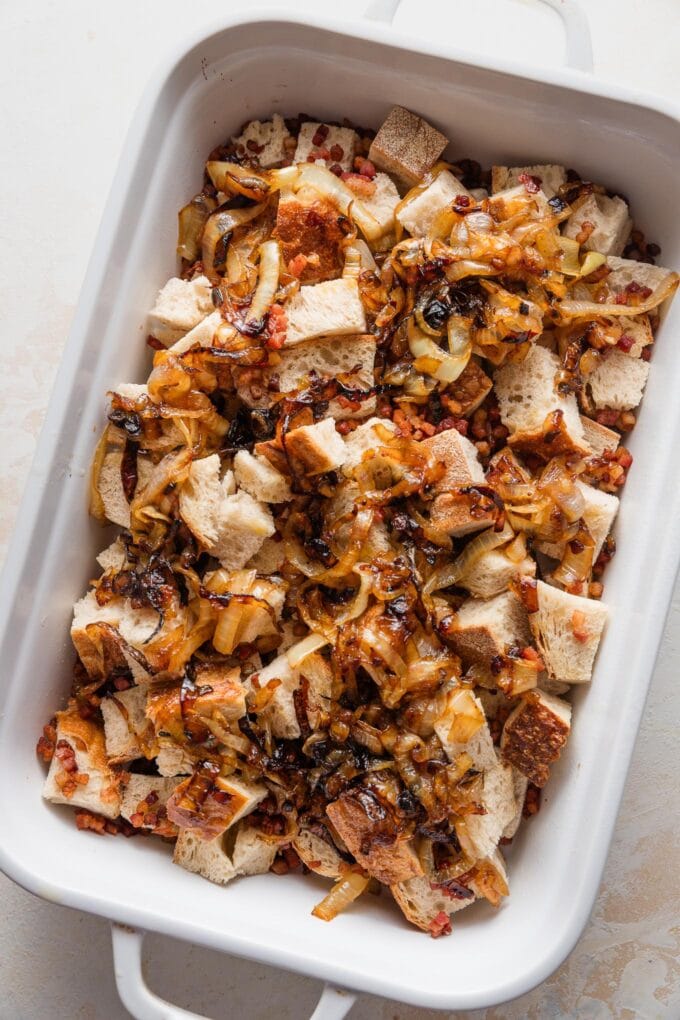 Caramelized onions spread over pancetta and bread cubes in a pan.