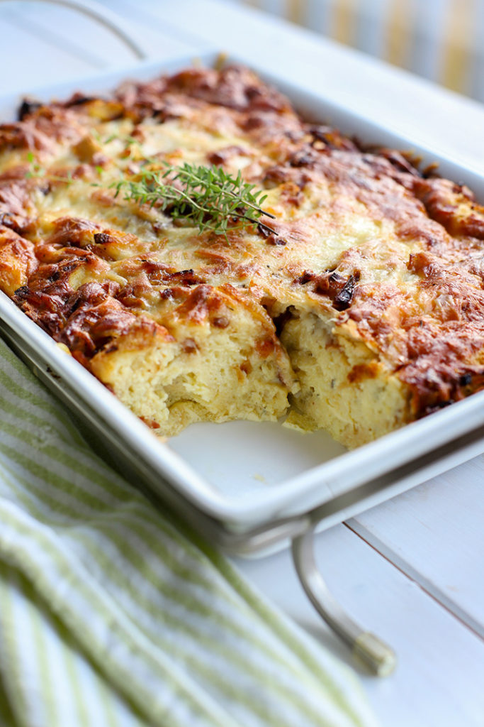 A large pan of breakfast strata with one slice removed from a corner.