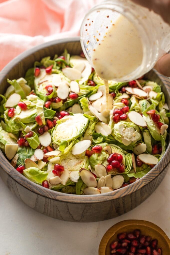 Close-up of a hand pouring buttermilk dressing over salad.