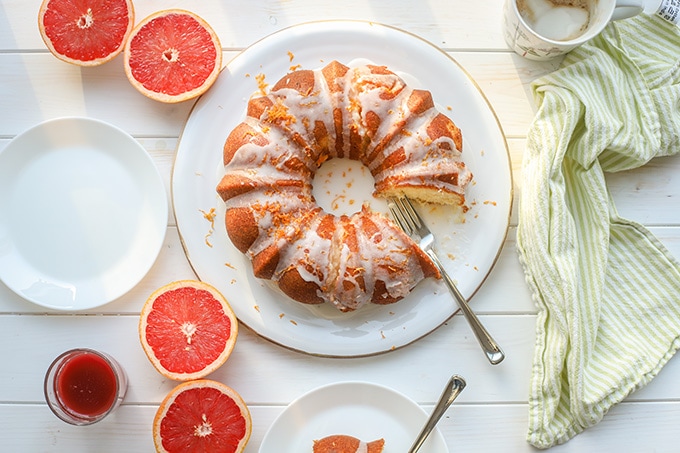 Flat-lay photo of glazed grapefruit bundt cake, cut and served with coffee, fresh grapefruit, and juice.