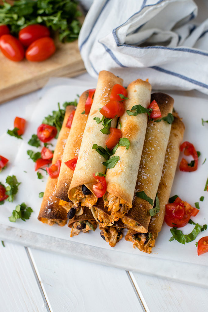A white tray filled with oven-baked chicken black bean taquitos.