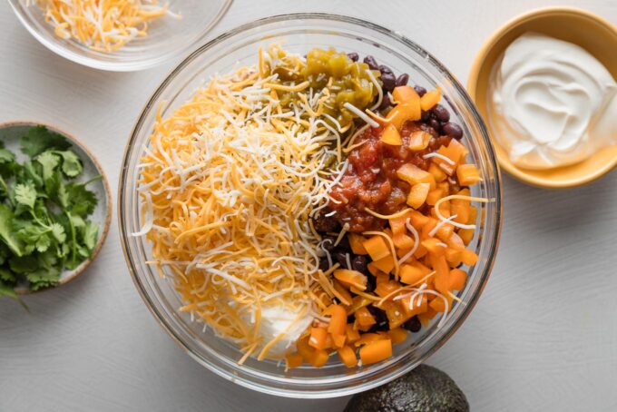 Clear glass prep bowl filled with shredded chicken, cheese, veggies, black beans, and spices.