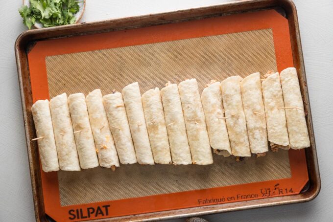 Rolled taquitos arranged on a baking tray.