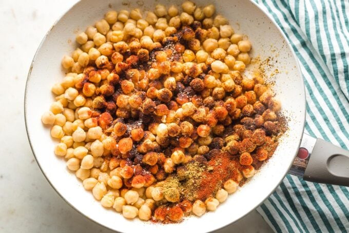 Chickpeas in a skillet with seasoning sprinkled on top.