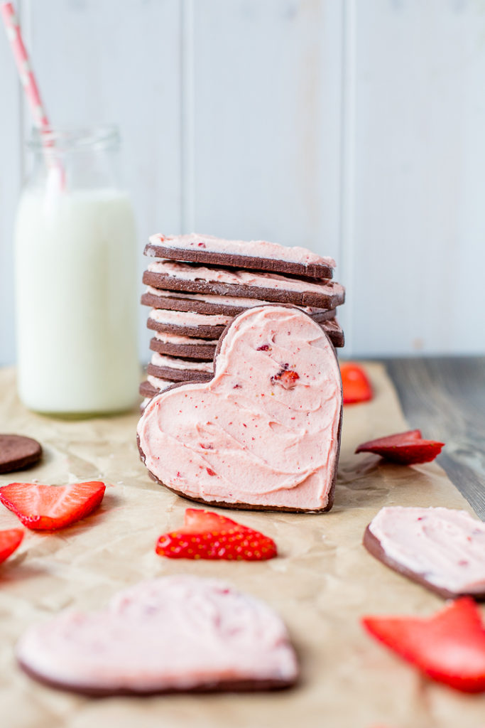 Heart-shaped chocolate sugar cookies stacked tall with a glass of cold milk in the background.