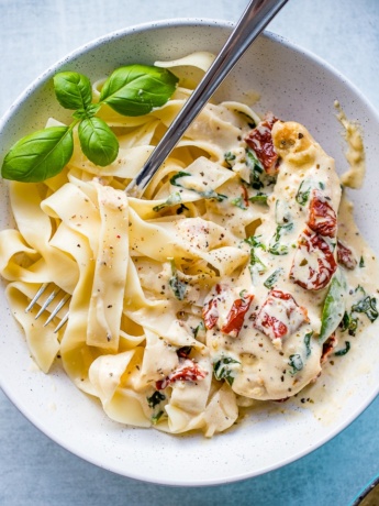 Close-up of a bowl filled with fettuccine and creamy Tuscan chicken with sauce, spinach, and sun-dried tomatoes.