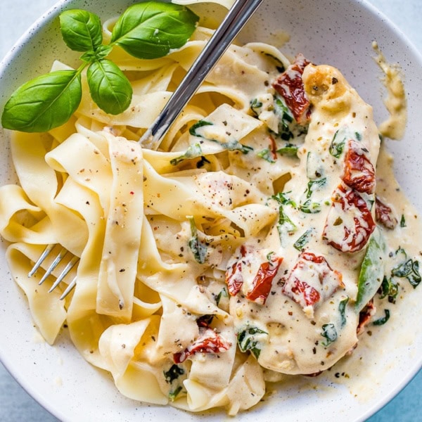 Close-up of a bowl filled with fettuccine and creamy Tuscan chicken with sauce, spinach, and sun-dried tomatoes.