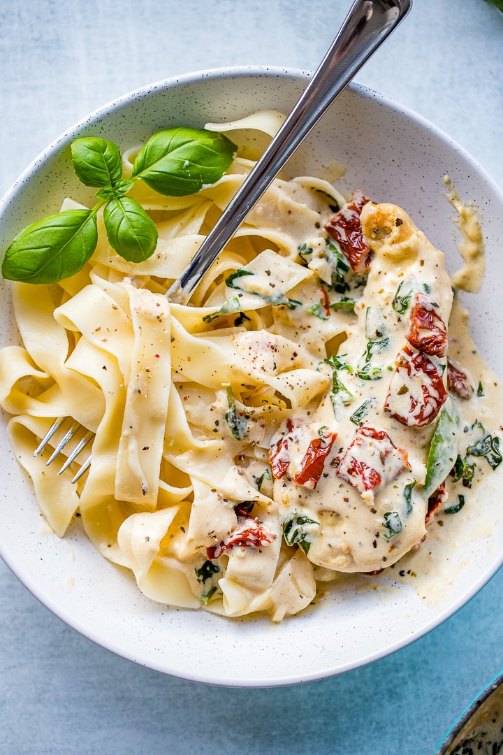 Close-up of a bowl filled with fettuccine and creamy Tuscan chicken with sauce, spinach, and sun-dried tomatoes.