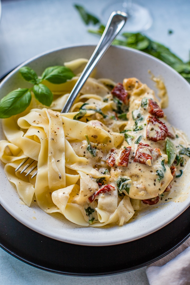 Close-up of creamy Tuscan chicken, ready to eat with a fork on the plate.