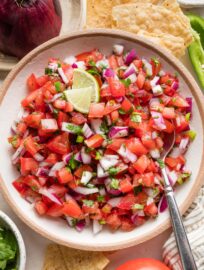 Bowl of homemade pico de gallo surrounded by tortilla chips, extra onion, and extra cilantro.