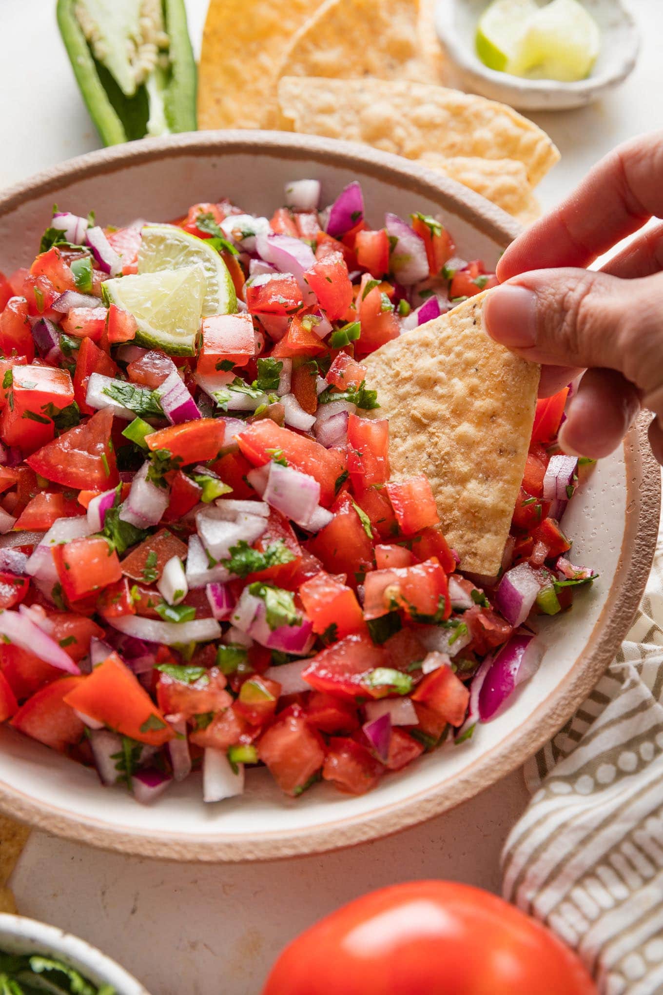 Woman's hand using a tortilla chip to scoop freshly homemade pico de gallo out of a bowl.