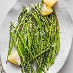 Oval ceramic plate piled with roasted lemon asparagus served with Parmesan and extra lemon wedges.