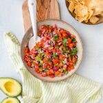 A bowl full of homemade pico de gallo, with chips, avocado, and a cold beer.