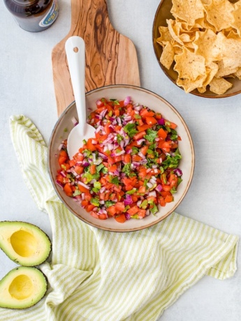 A bowl full of homemade pico de gallo, with chips, avocado, and a cold beer.