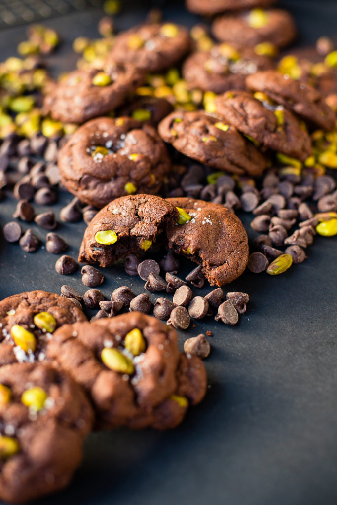 A pile of sea salt pistachio chocolate chip cookies, with one cookie broken apart.