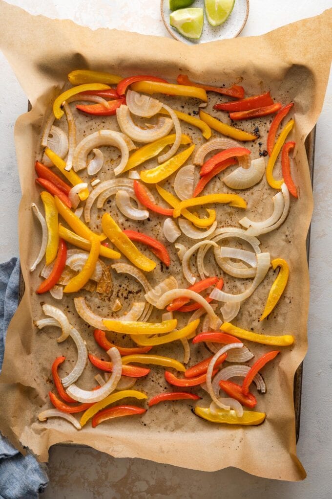 Large sheet pan lined with parchment paper and filled with thinly-sliced bell pepper and onion.