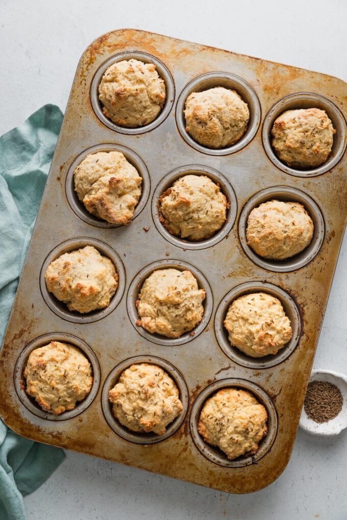 Overhead view of a metal muffin tin filled with soda bread muffins, with craggy, golden brown tops and just removed from the oven.