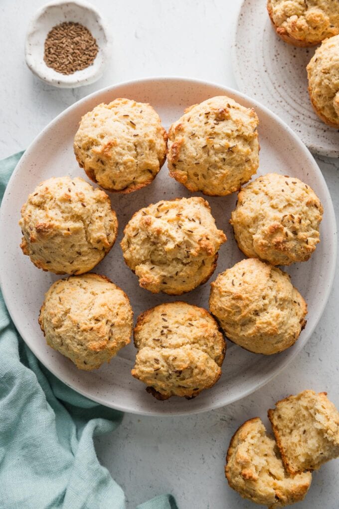 White plate filled with a batch of soda bread muffins made with caraway seeds.