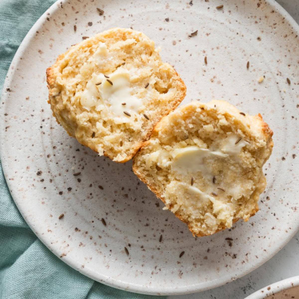 Close up of a soda bread muffin with caraway seeds split open and slathered with butter.
