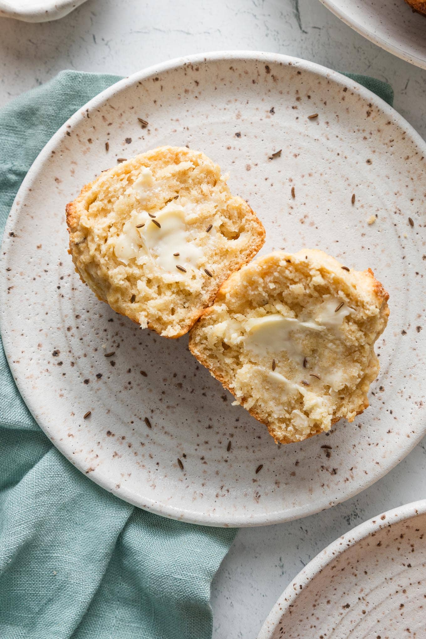 Close up of a soda bread muffin with caraway seeds split open and slathered with butter.