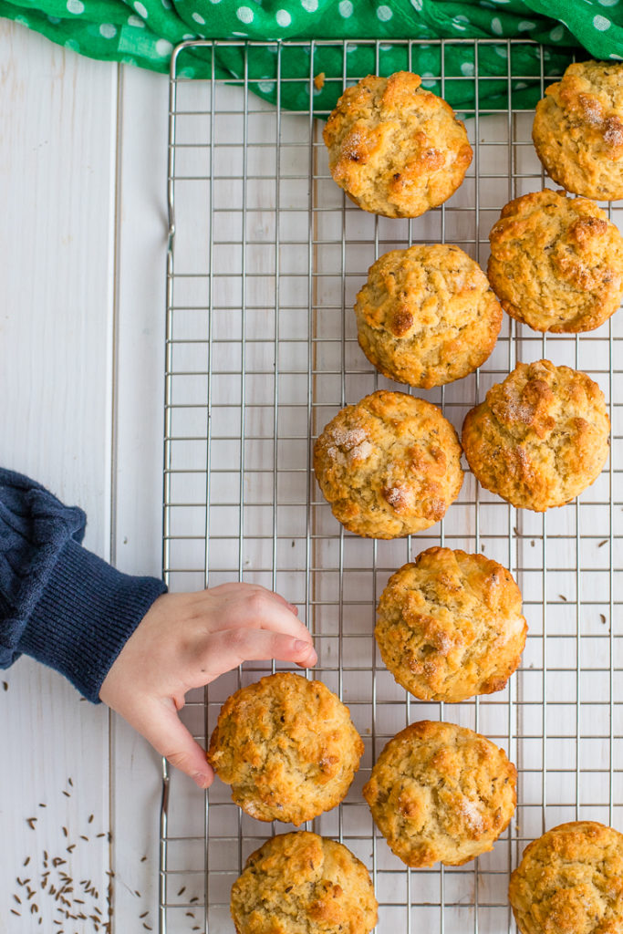 Flat lay with a toddler's hand reaching into the frame to grab one muffin off of a cooling rack.