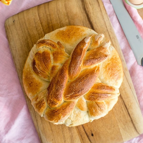 Flat-lay of a loaf of homemade paska with a cross on top, with tulips and eggs in the background.