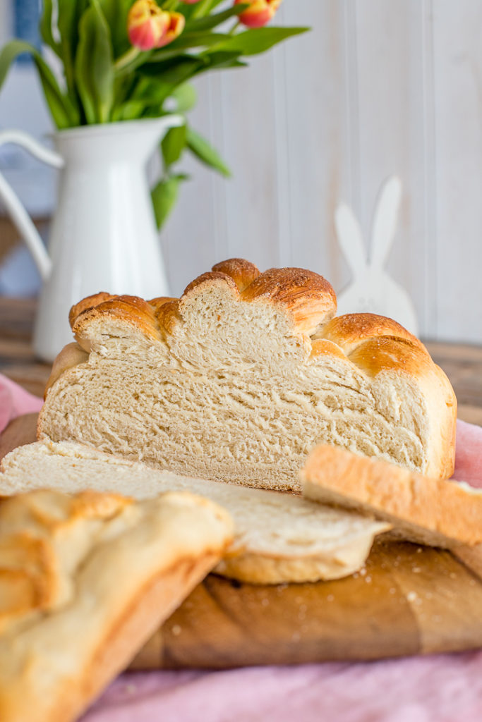 A cut-open loaf of paska, with slices arrayed in front, and a vase of flowers and decorative bunny in the background.