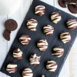 A slate serving tray arranged with neat rows of Irish cream Oreo truffles dipped in white and dark chocolate.