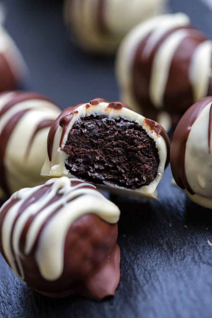 A slate serving tray stacked with Irish cream Oreo truffles dipped in dark and white chocolate, one stacked with a bite out of it.