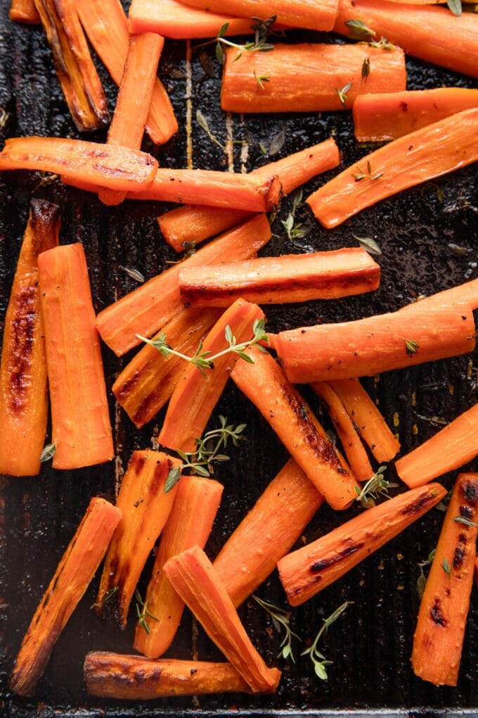 Close up of roasted carrots with thyme on a small sheet pan.