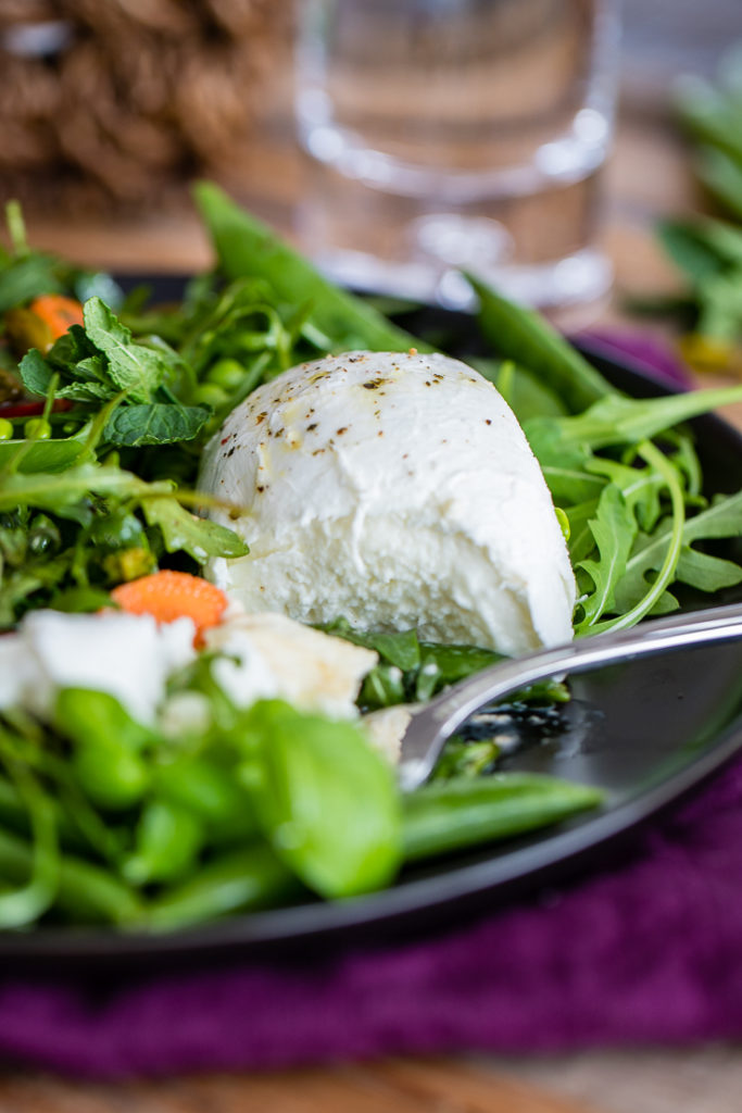 Close-up of a cut-open ball of fresh Buffalo mozzarella cheese nestled in a bright salad of arugula and sugar snap peas.