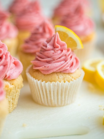 Close-up of a lemon cupcake topped with fresh strawberry frosting and a fresh lemon slice.