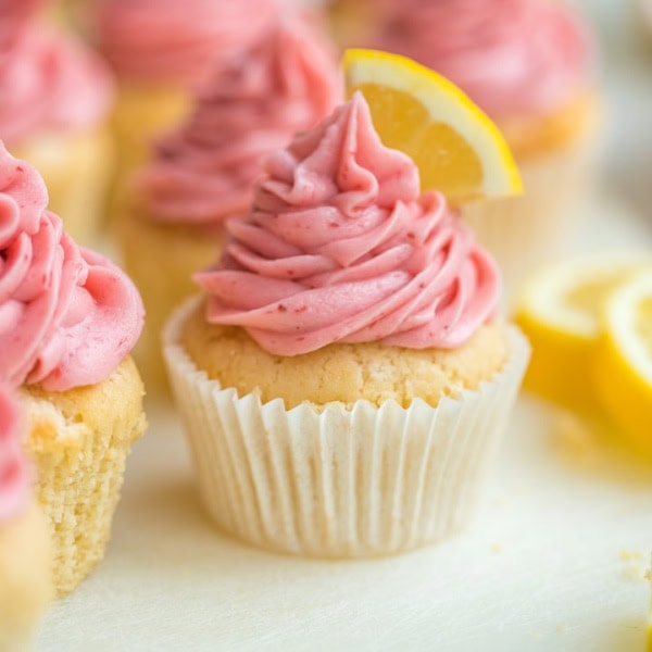 Close-up of a lemon cupcake topped with fresh strawberry frosting and a fresh lemon slice.