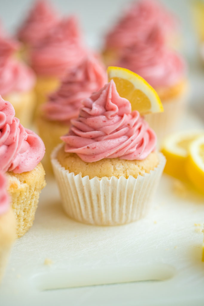 Close-up of a lemon cupcake topped with fresh strawberry frosting and a fresh lemon slice.